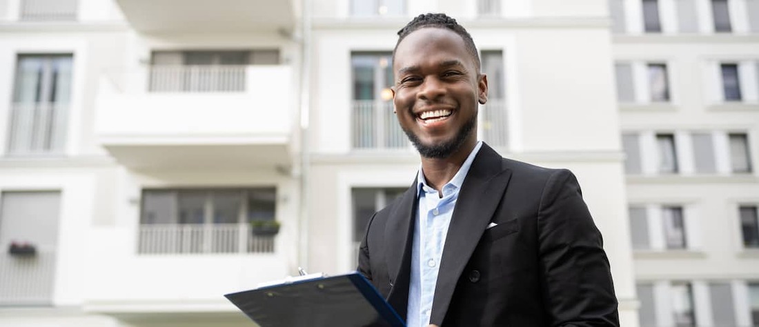 An African. American real estate. agent standing outside apartments.