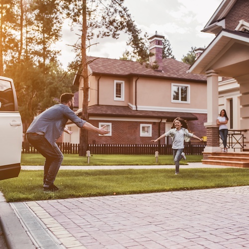 Young girl running towards her father across their front lawn.