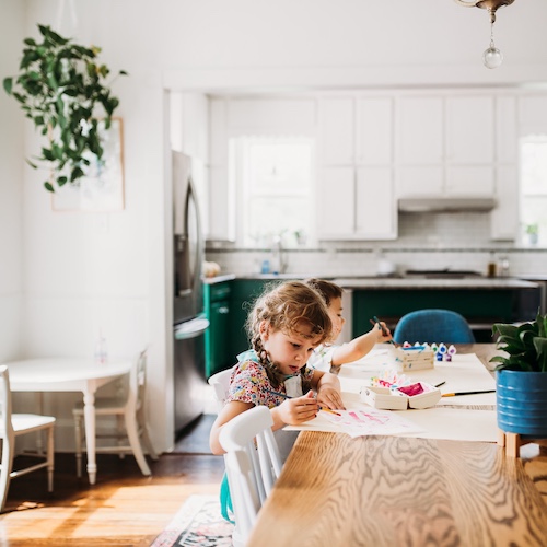 Young kids doing art project at large dining room table in open, airy and sun filled room.