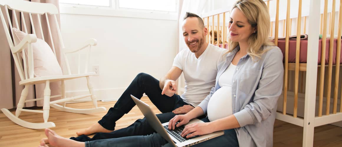 Young couple with a pregnant wife sitting in a new nursery using a laptop.