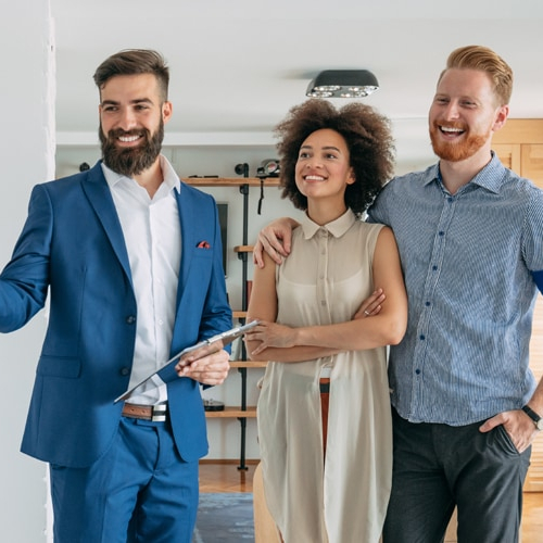 A real estate agent with a clipboard in hand showing house to a couple.