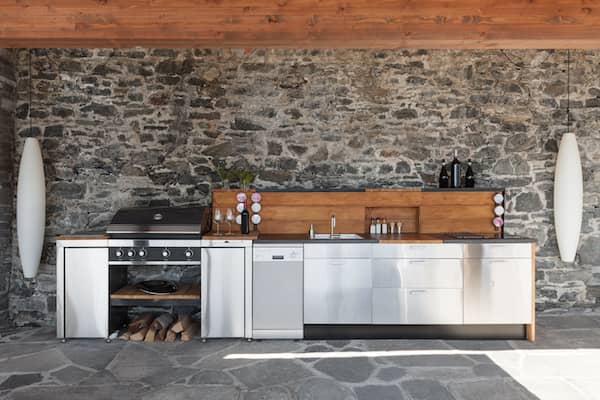 Modern style outdoor kitchen along a stone wall with long vertical lights on either side.