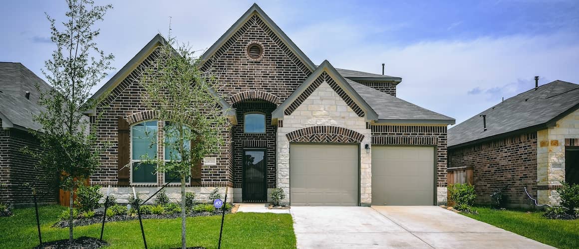 Large Texas home with two garages and two saplings in front lawn.