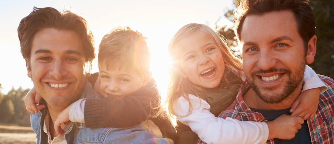 Dads giving backrides to their young kids at sunset, smiling.