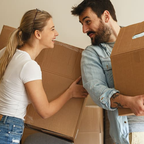 Image depicting a couple during the process of moving into a new home, with boxes and furniture being transported.