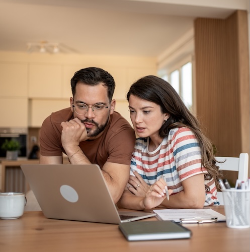 Young couple looking at computer screen with concern, as if they've received a mortgage denial.