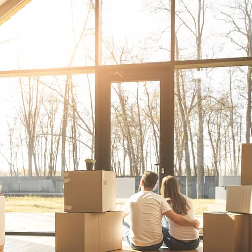 A couple enjoying sunlight in their newly bought home surrounded by cardboard boxes.