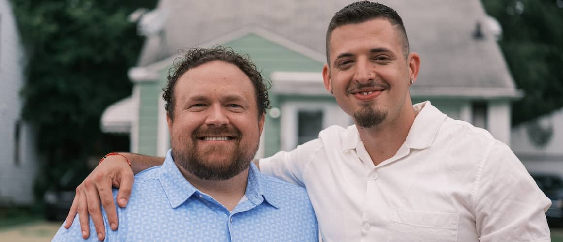 Two men smiling in front of home.