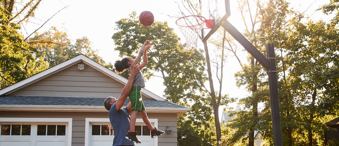 RHB Assets From IGX: Dad and child playing basketball together in a suburban driveway.