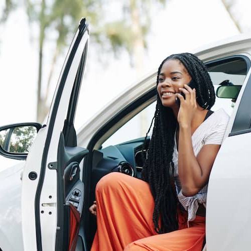 Young woman chatting on phone and getting out of her white new car.
