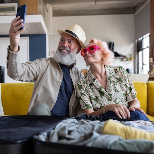 Senior couple taking selfie while packing for vacation home travel.