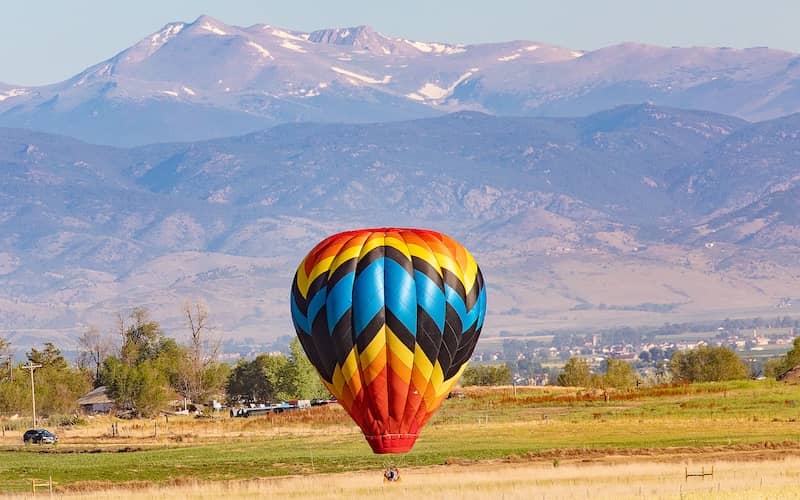 Hot air balloon in rich, beautiful colors of red, orange, yellow and blue with mountains in the background. 