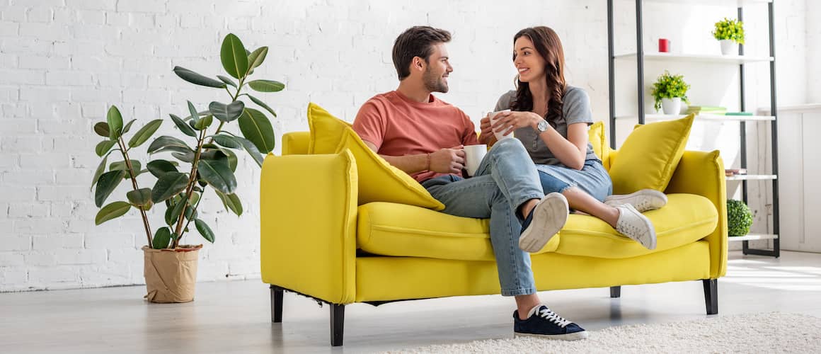 A happy young couple sitting on a yellow sofa.