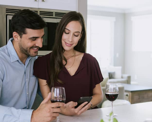 Image of man and woman looking down at phone in kitchen, smiling.