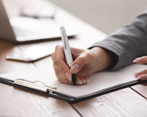 Woman writing down checklist on clipboard on her desk.