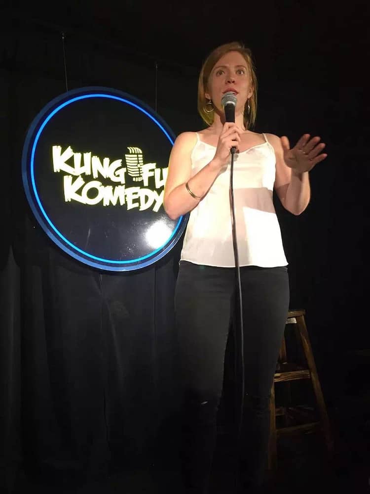 Woman doing stand-up comedy in Shanghai in front of a sign that reads "Kung Fu Komedy.".
