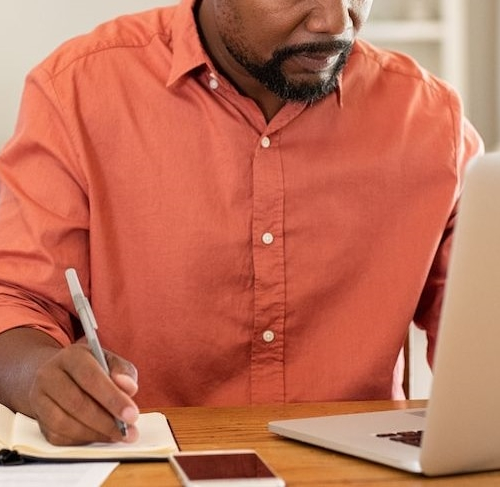 Man writing finances in a notebook, indicating budgeting or financial planning.