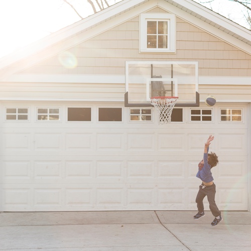 Young boy playing basketball on garage hoop.