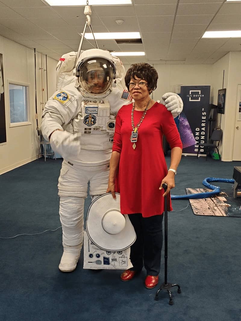 Woman with cane standing beside a man in an astronaut uniform.