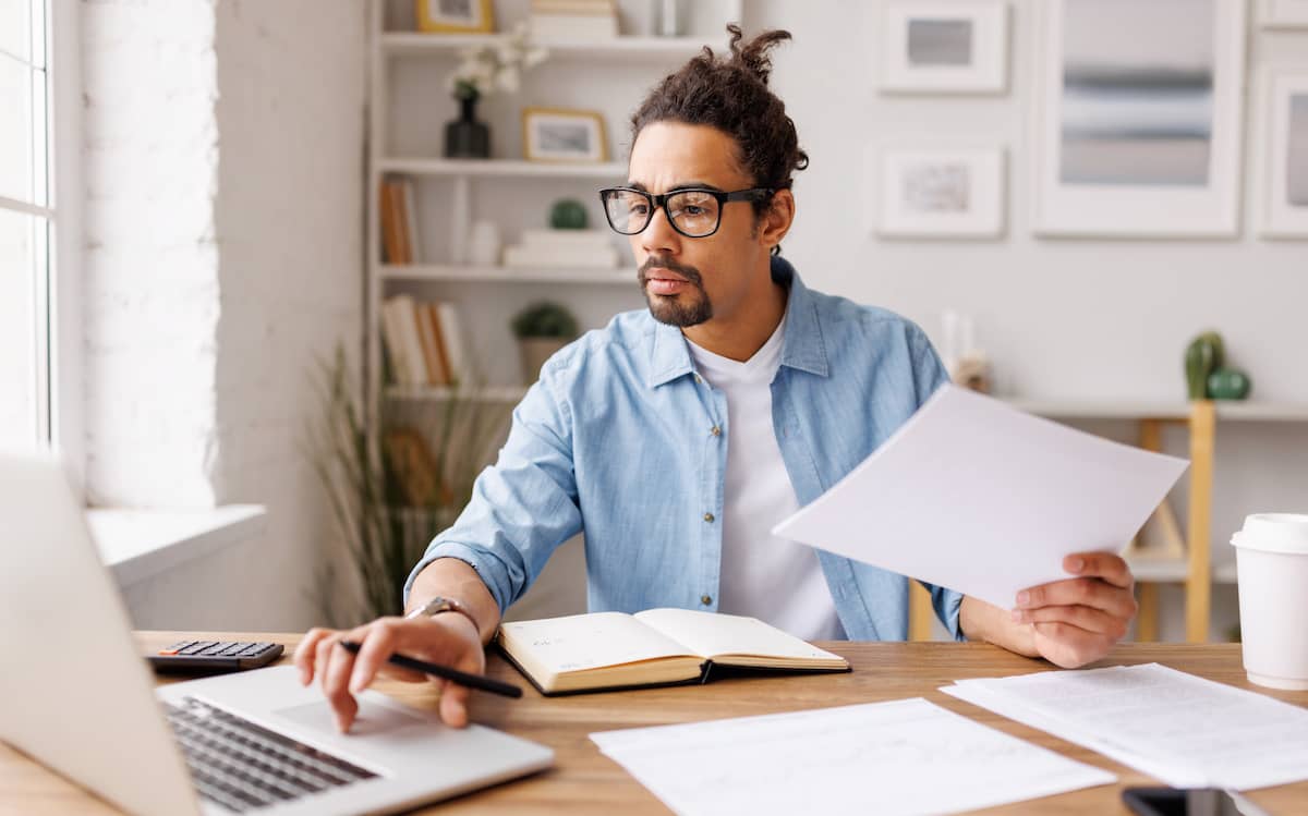 Man reading documents in front of laptop.