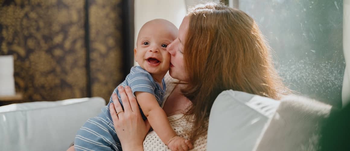 Mother kissing baby on cheek at home on couch.