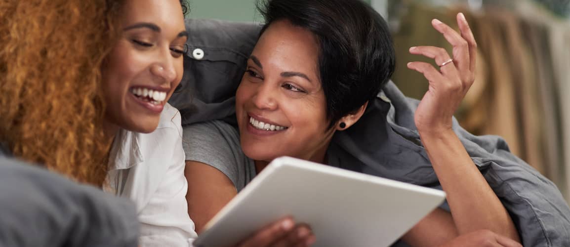 A young lesbian couple using a tablet in bed, representing modern lifestyle and technology use.