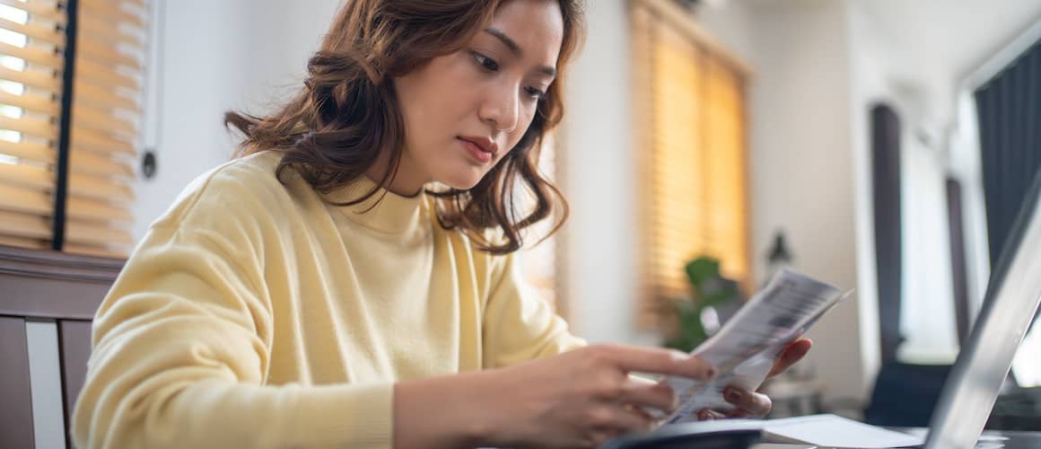 Woman calculating finances with calculator and laptop at home office desk.