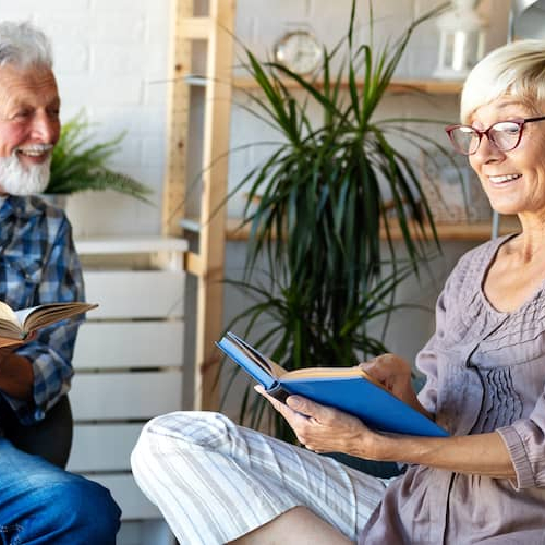 An elderly couple sitting and reading together having a good time.