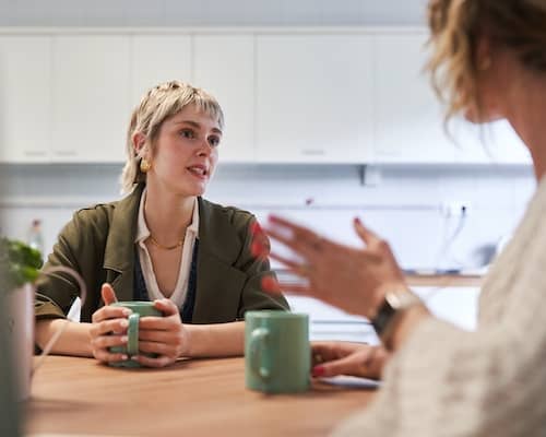 Two women conversing over coffee at a dining room table.