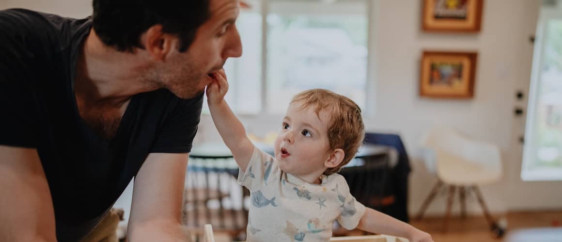 Father with young child eating together in kitchen.