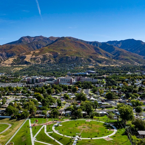 Aerial view of Ogden City in Utah featuring a large park and distant mountains.