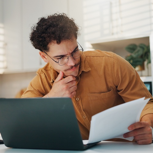 Young man looking at some documents while sitting in front of a laptop.