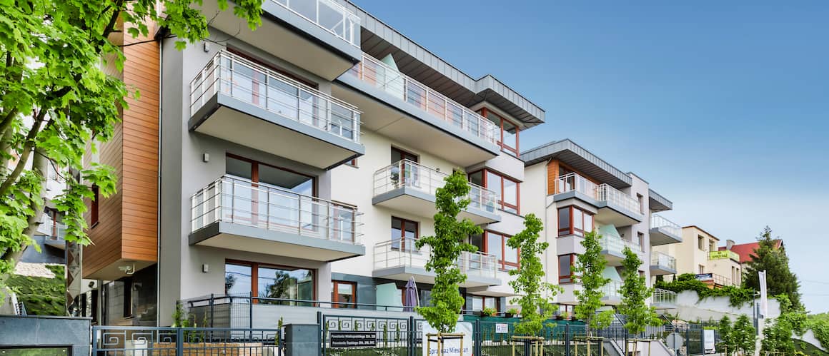 Image of a tall, new apartment building with balconies and greenery around the grounds.