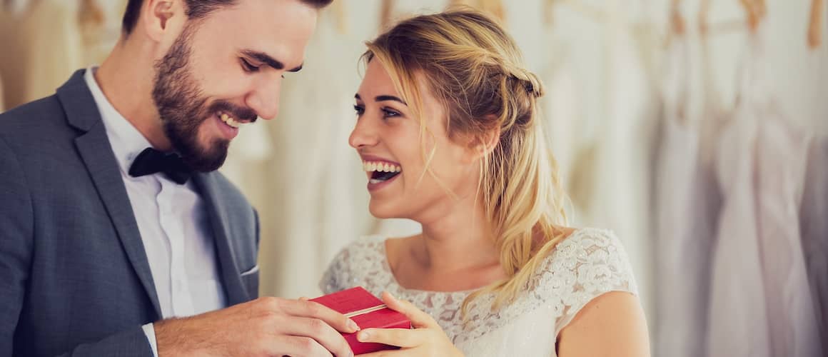 couple in wedding attire smiling and laughing holding red box