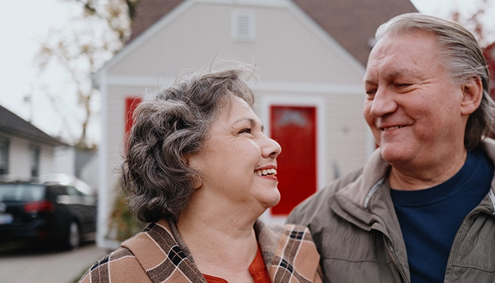 Couple standing in front of house with red door smiling at each other.
