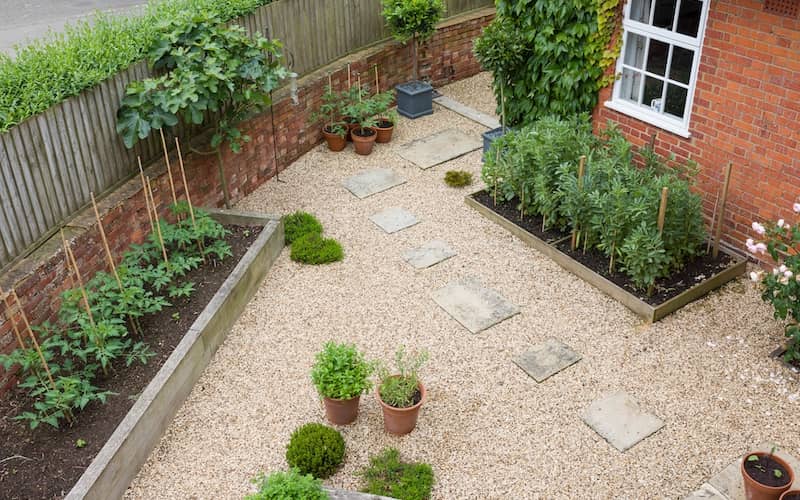 Backyard garden using mixed materials of stone, a pathway made of pavers, flowerpots and raised bed gardens. 