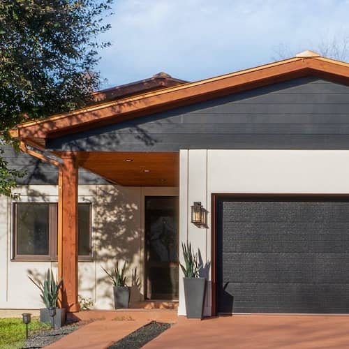 Ranch style home in Contemporary style with wood framing, black garage door and front door and white exterior.