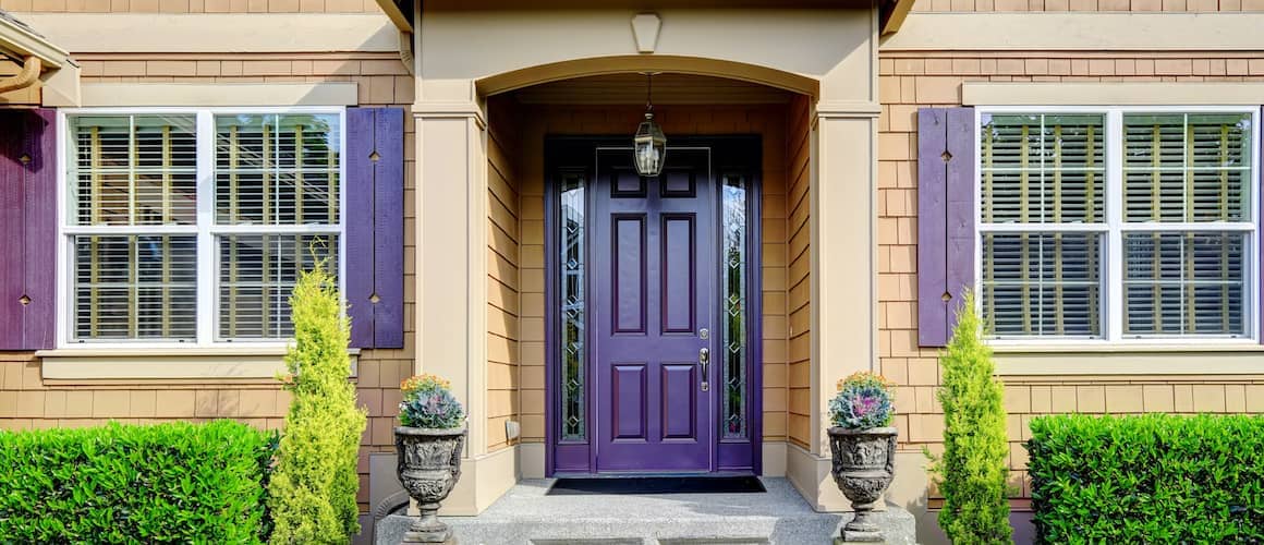 Front entrance to a tan colored house with dark purple window shutters and a dark purple door.