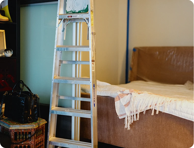 Ladder next to a bed with a fringed blanket in a room that appears to be in progress.