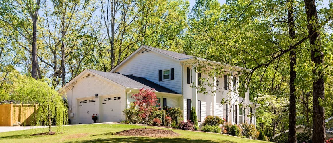 Large American home sitting on a hill surrounded by many trees.