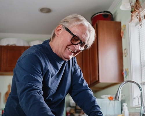 Man with glasses smiling while putting coffee cup in the dishwasher.
