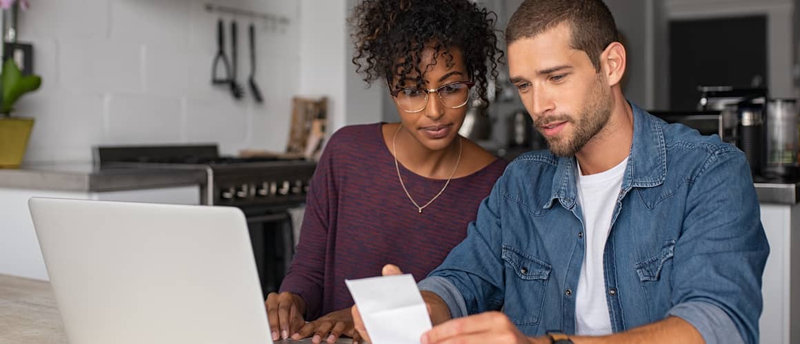 Young couple reviewing finances using a laptop computer and receipts.