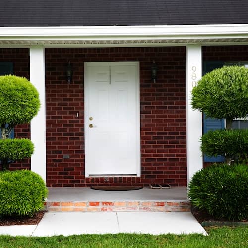 Front door of brick ranch house with topiary shrubs on either side.