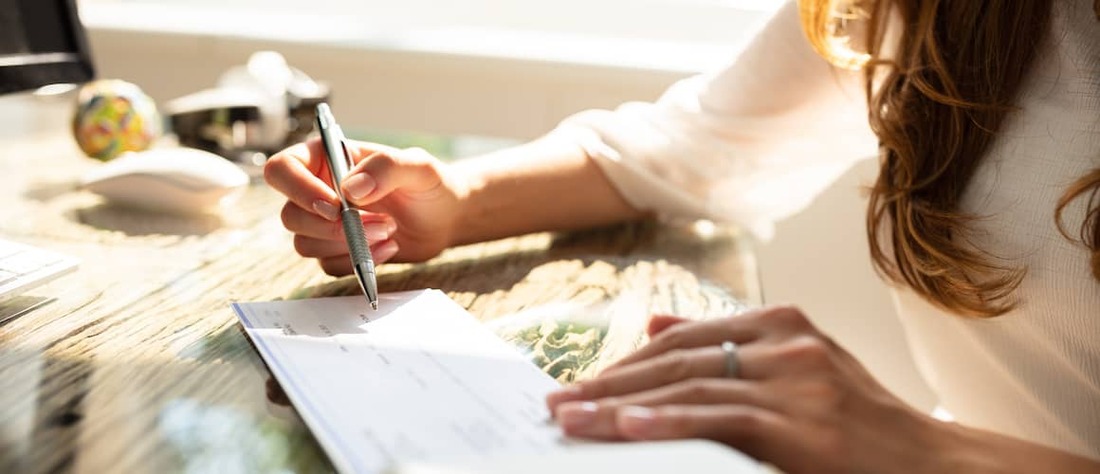 Woman writing a check on her desk.