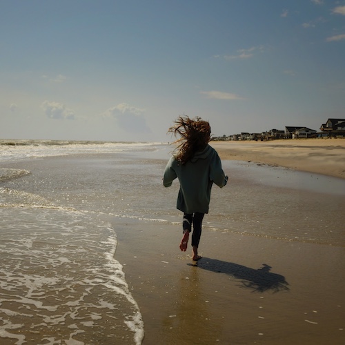 Young girl running along beach on Atalantic Ocean with properties in the distance.