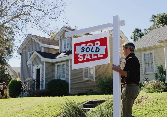 Person standing beside a sold sign in front of a home