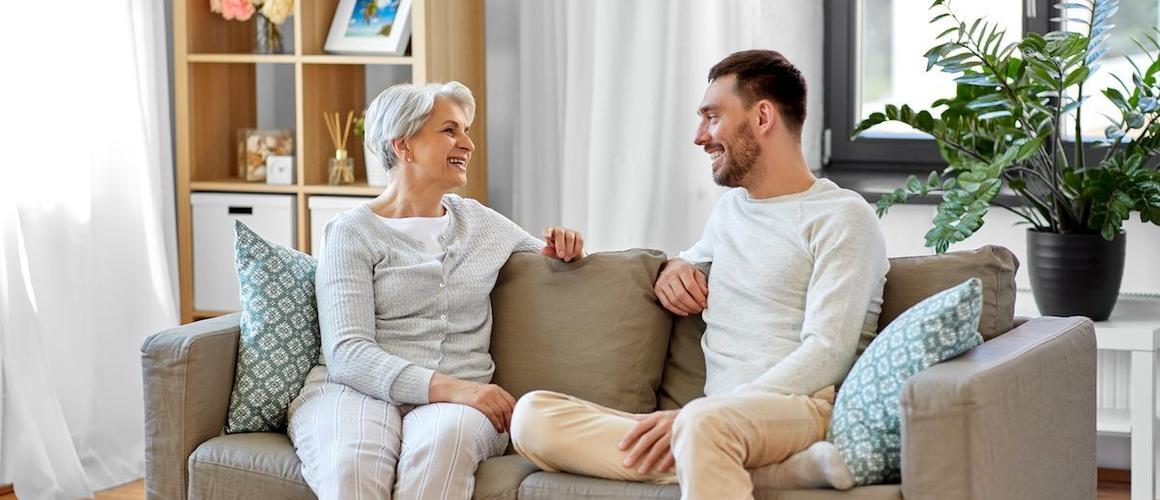 RHB Assets From IGX: Older mother and adult son talking and smiling in a living room.