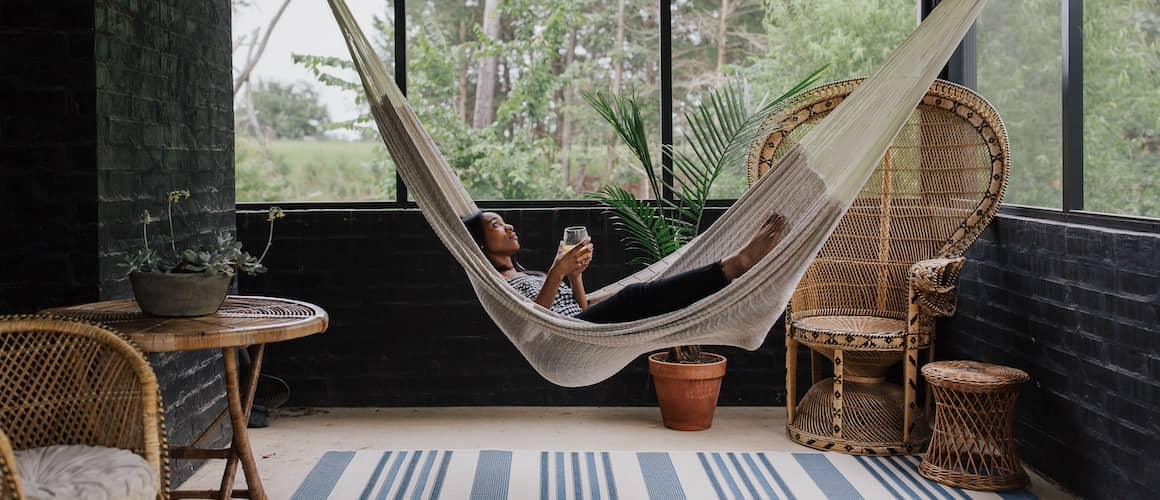 Woman laying in hammock hanging in enclosed sun porch surrounded by trees.