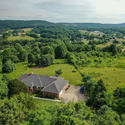 Aerial view of large home in Cookville, Tennessee in a wooded valley with mountains in the distance.