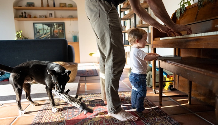 Father playing piano with small child and dog nearby.